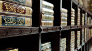 رفوف خشبية تحتوي على مجموعة من الكتب التقليدية ذات الغلاف الملون والكتابات العربية، تظهر تفاصيلها الزخرفية.
